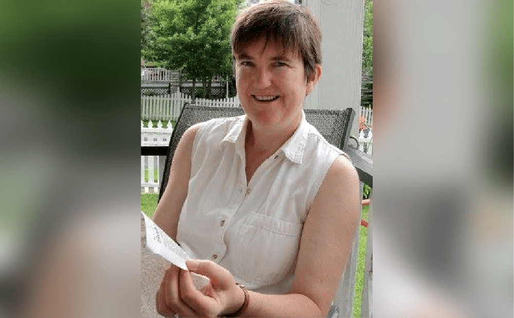 A woman is smiling while holding a piece of paper.