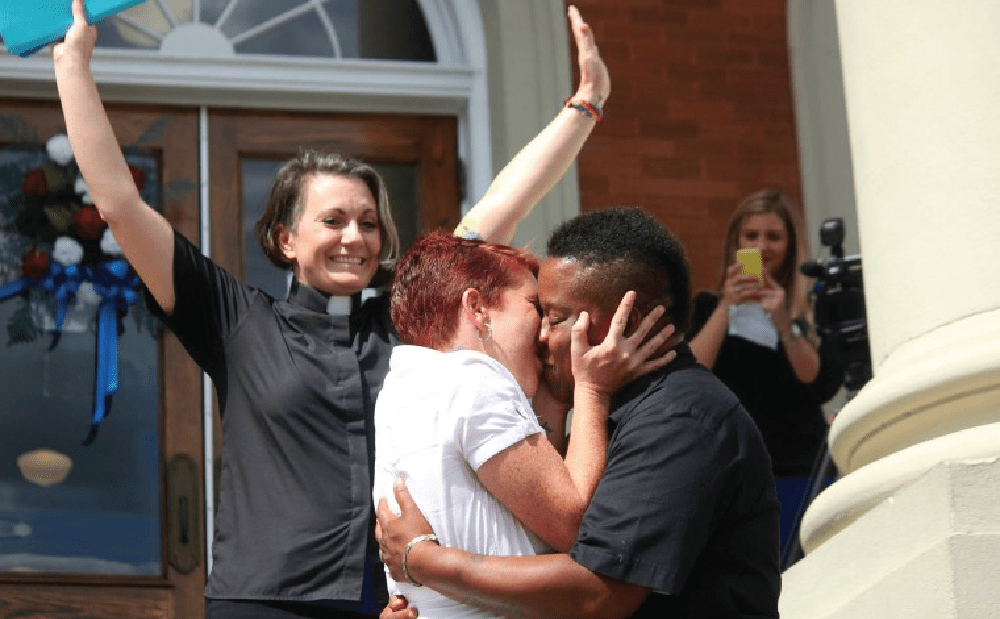 A couple kisses in front of a church.