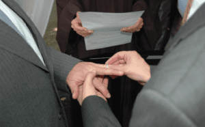 A man is putting a wedding ring on another man's finger.