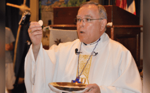 A priest in a white robe holding a bowl.