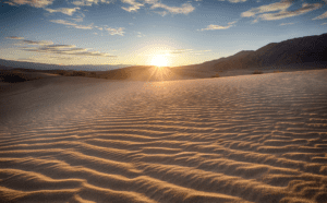 The sun is setting over a sand dune.