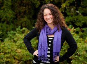 A woman with curly hair and purple scarf posing for a photo.