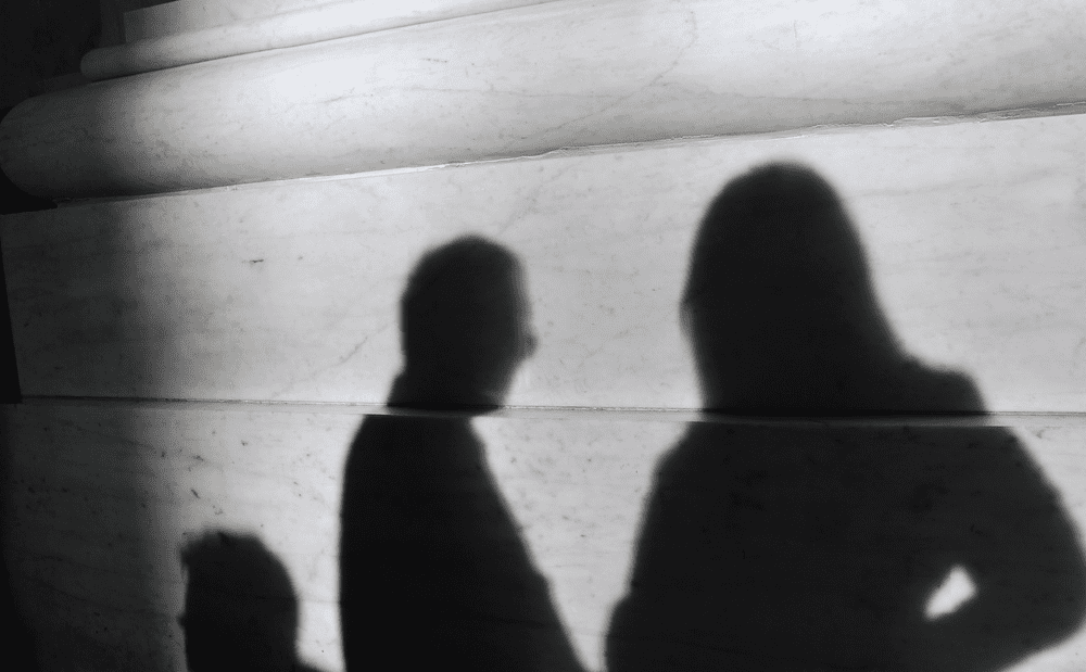 Shadows of two people standing in front of a pillar.