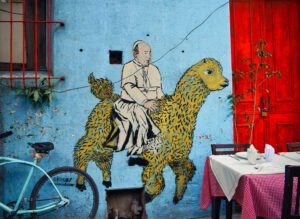 A painting of a man riding a llama on a blue wall.