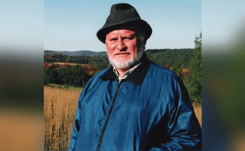 An older man in a blue jacket and hat standing in a field.