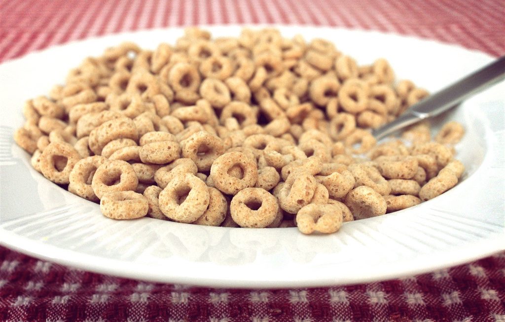 A bowl of cereal with a spoon on a red and white checkered tablecloth.