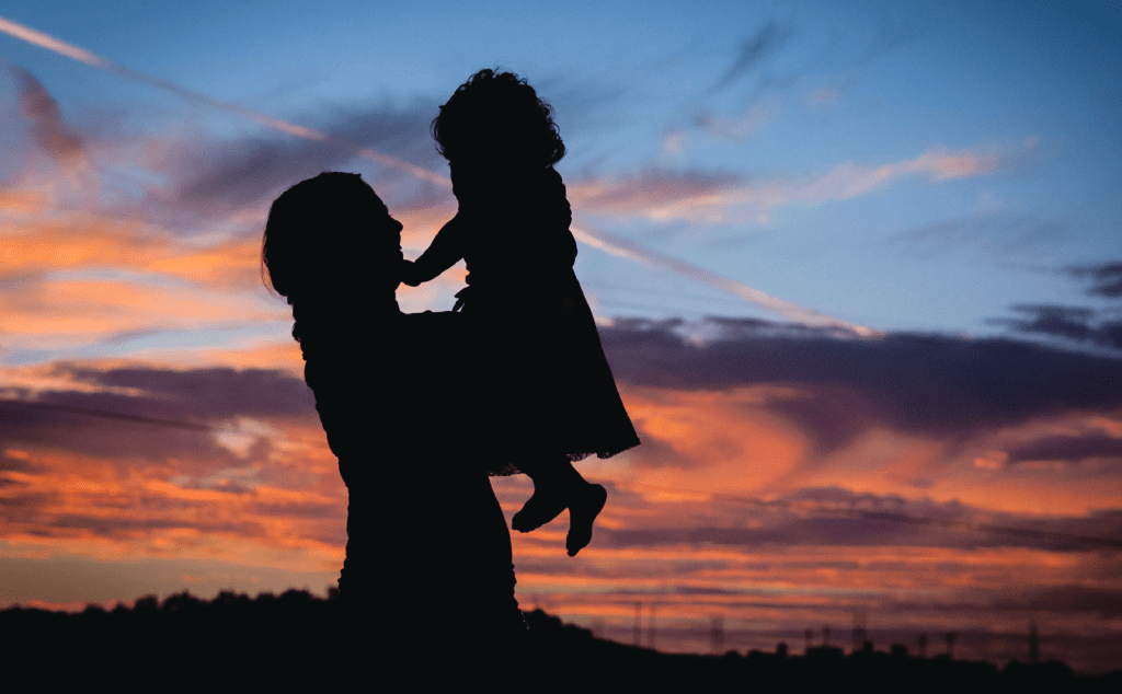 A silhouette of a woman holding a child at sunset.