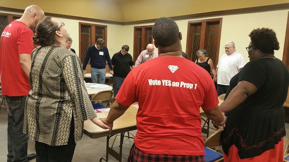 A group of people in red shirts standing around a table.