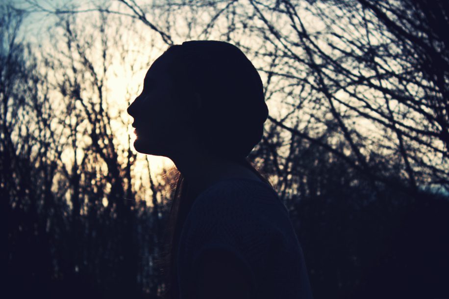 A silhouette of a woman in the woods at sunset.