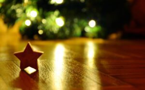 A wooden star sits on a wooden floor next to a christmas tree.