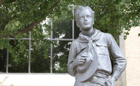 A statue of a boy scout in front of a building.