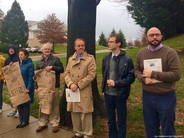 A group of people holding signs in front of a tree.