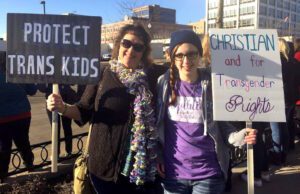 Two women holding signs that say protect christian trans kids.