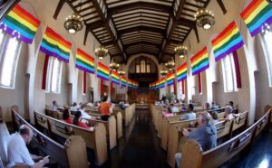 The inside of a church with rainbow flags hanging from the ceiling.