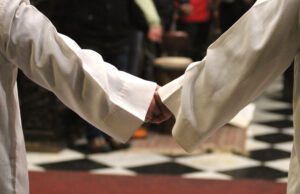 Two priests holding hands in front of a checkered floor.