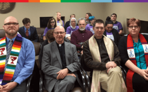 A group of people sitting in a room with a rainbow scarf.