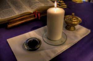 A candle sits on a table next to an open bible.