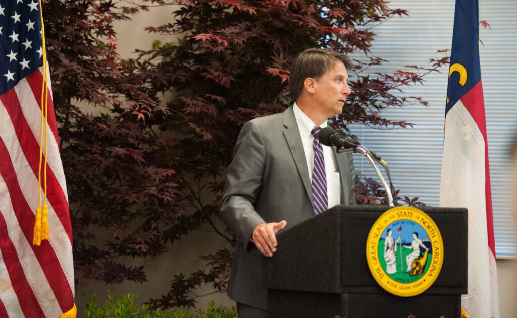 A man standing at a podium in front of an american flag.