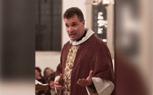 A priest in a red and maroon robe is giving a sermon.