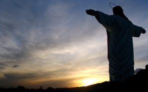 A statue of jesus with his arms outstretched at sunset.