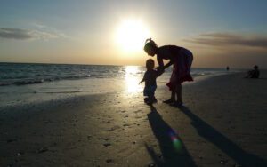 A woman and a child walking on a beach at sunset.