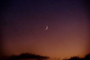 A crescent is seen in the sky at sunset.