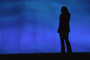 A silhouette of a woman standing in front of a blue wall.