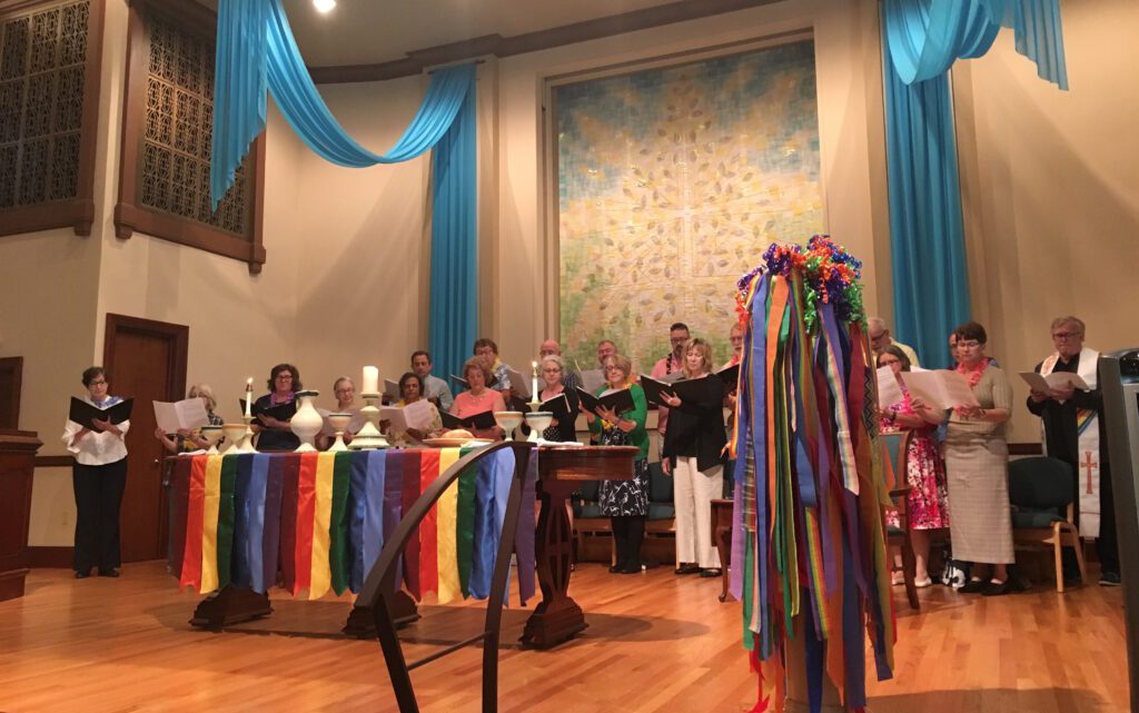 A group of people standing in front of a church with rainbow ribbons.