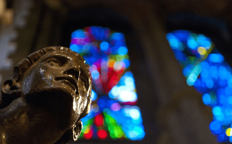 A statue of a man in front of a stained glass window.