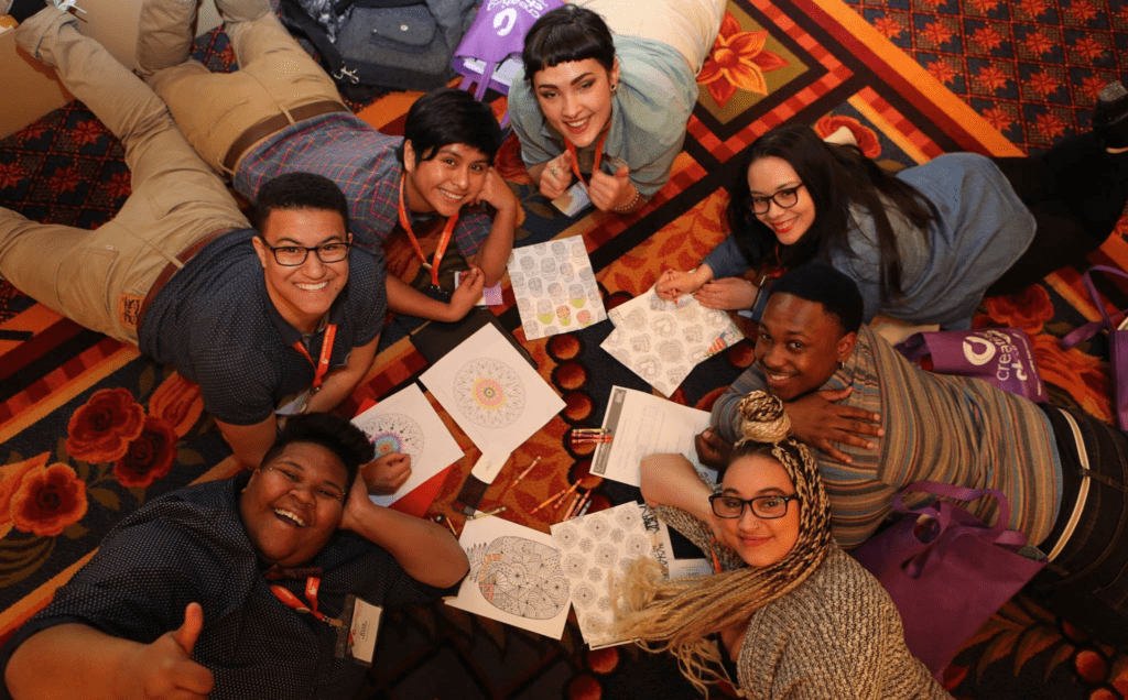 A group of people laying on a floor with pens and papers.