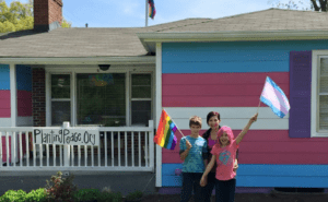 Three children standing in front of a house with a rainbow painted on it.