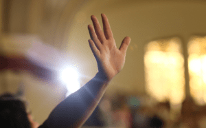 A person's hand is raised in front of a church.