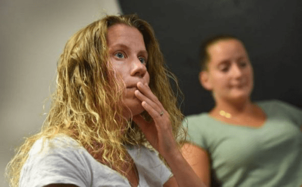 Two women are sitting in a room and one is looking at her phone.