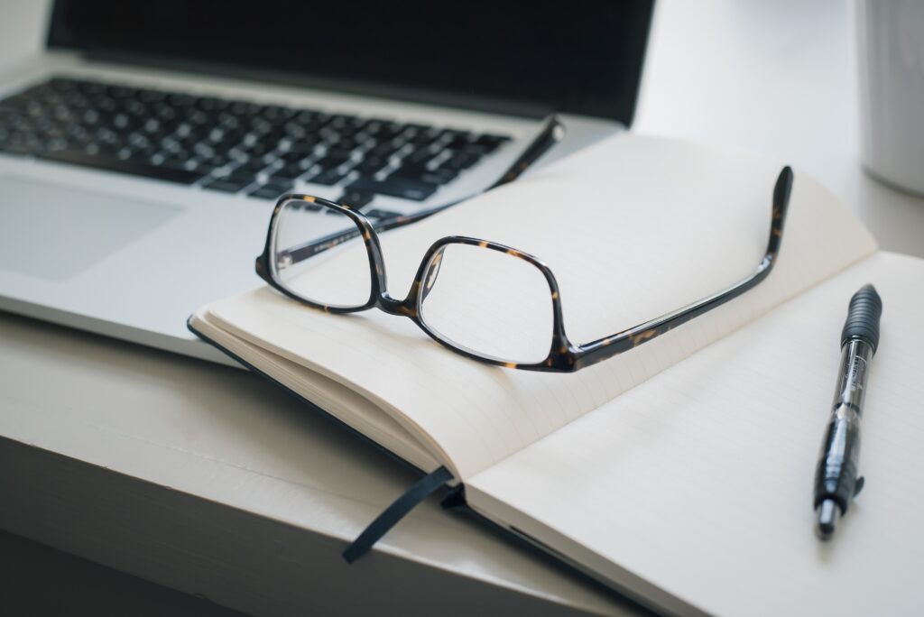 Eyeglasses on a notebook next to a laptop.