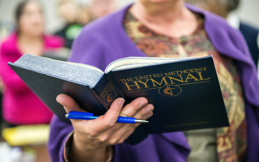 A woman holding a hymnal in front of a crowd.