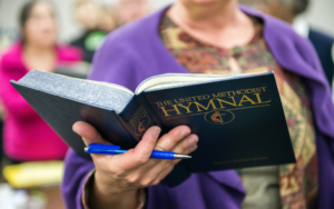 A woman holding a hymnal in front of a crowd.