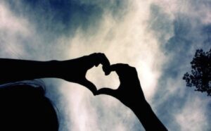 A silhouette of two hands making a heart shape.