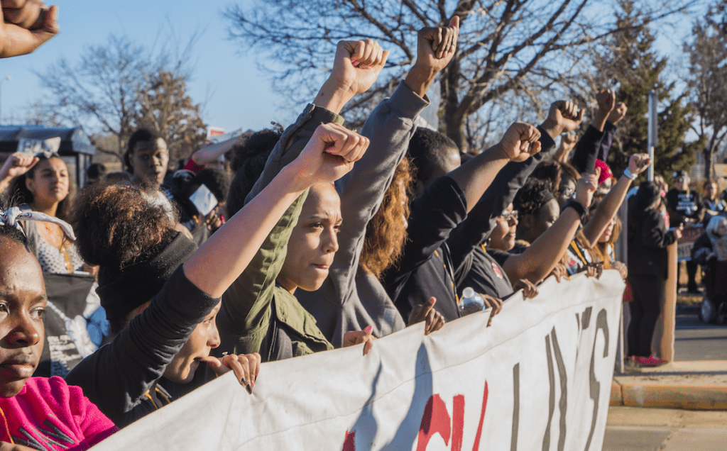 A group of people holding up a banner with their fists up.