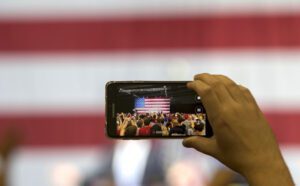 A person takes a picture of an american flag in front of a crowd.