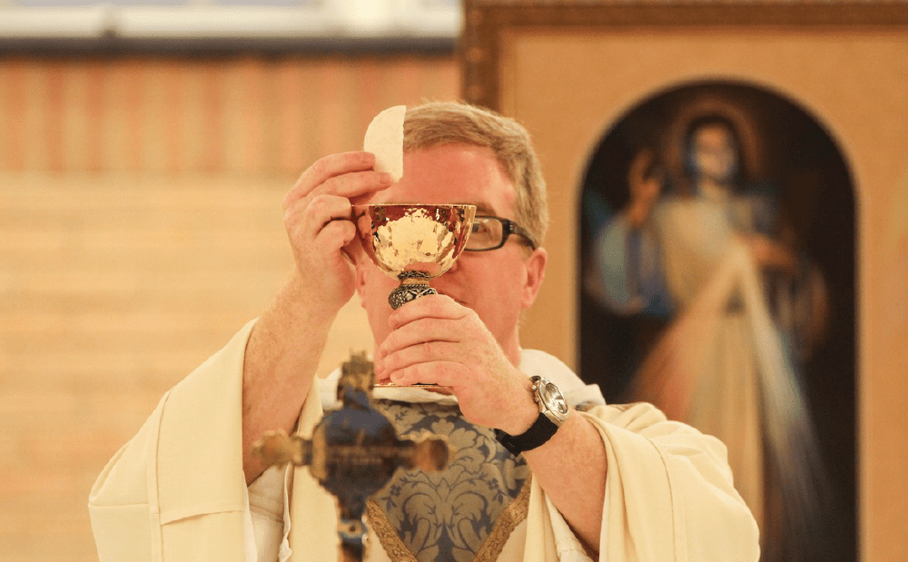 A priest is holding a cup in front of a painting.