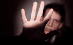 A man is holding his hand up in front of a dark background.