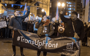A group of people holding a sign that says trans up front.