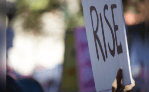A person holding up a sign that says rise.