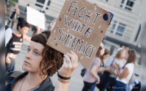 A woman holding up a sign that says fight white supremacy.