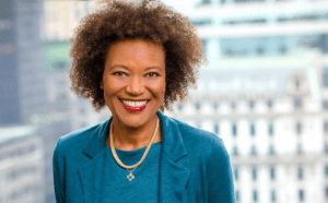 A woman with afro hair smiling in front of a city.