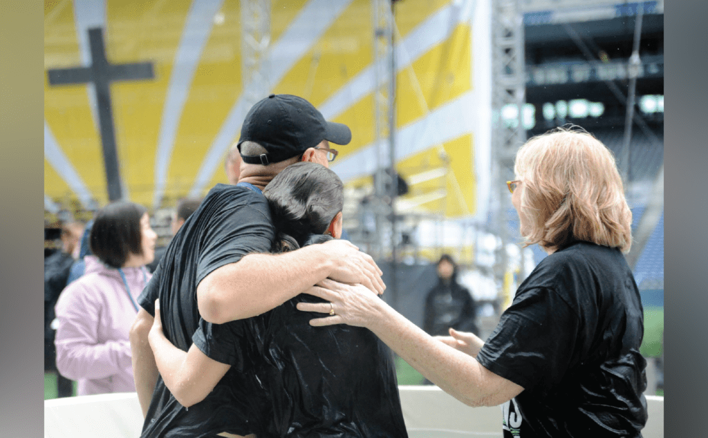 A group of people hugging in front of a cross.