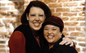Two women hugging in front of a brick wall.