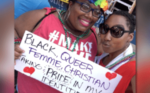 Two women holding up a sign that says black queer feminist christian.