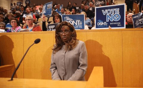 A woman standing at a podium in front of a crowd of people.