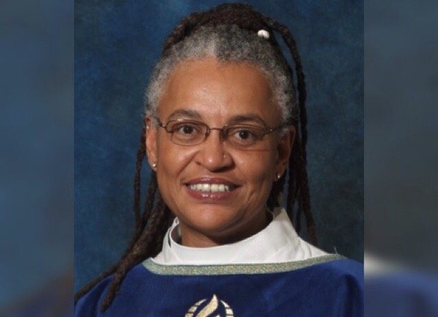 A woman in a blue robe with dreadlocks smiling.